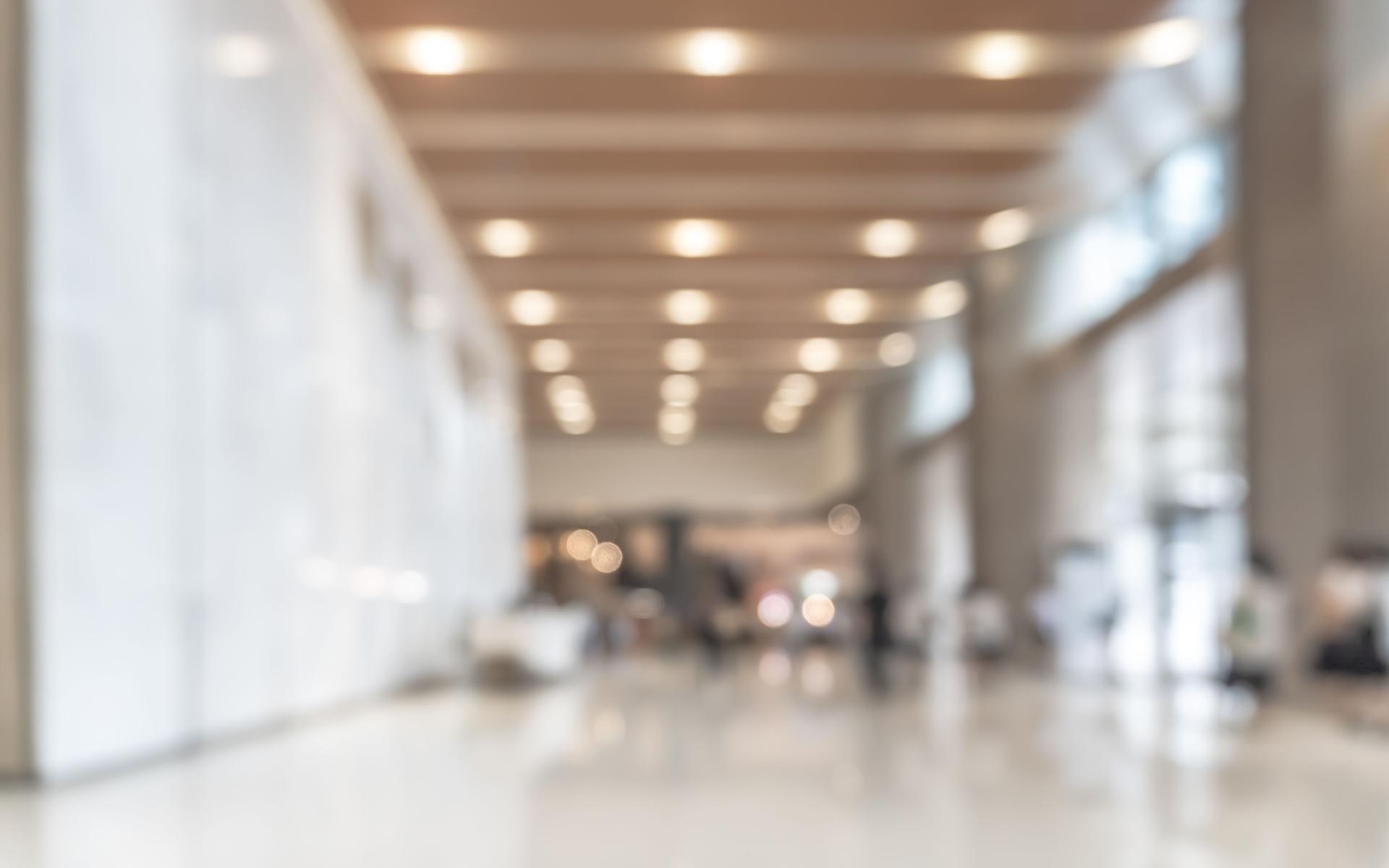 Blurred office building lobby or hotel blur background interior view toward reception hall, modern luxury lounge, white room space with blurry corridor and building glass wall